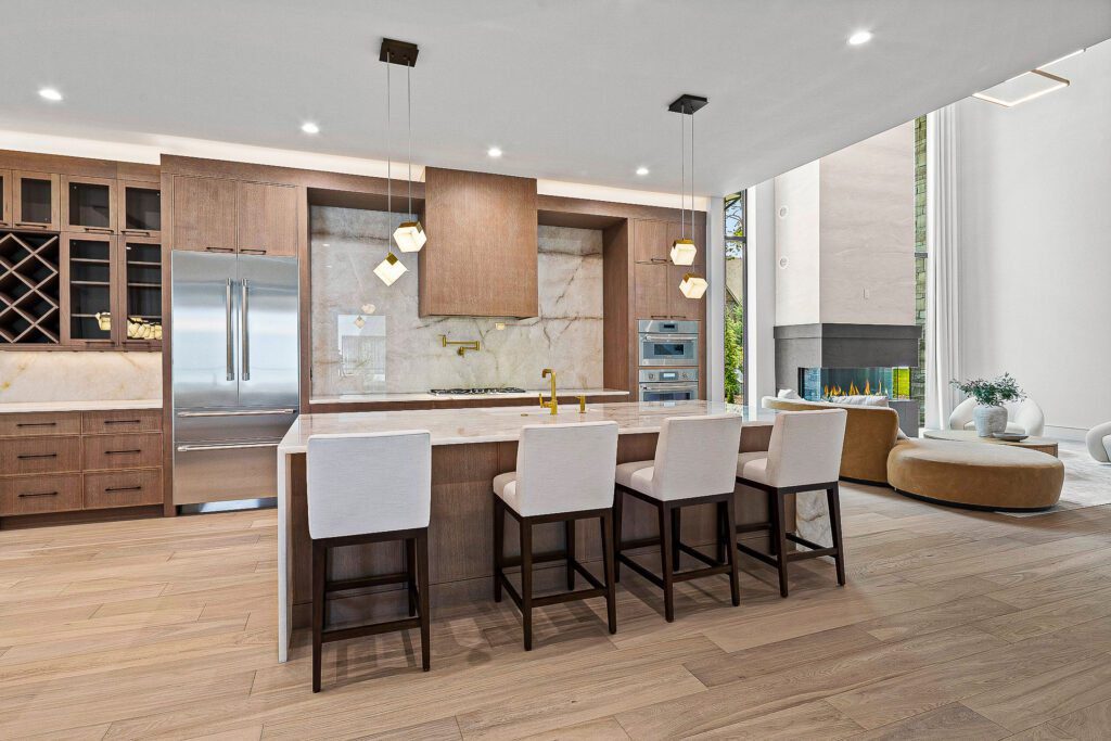 Custom kitchen with warm wood cabinetry and a natural stone slab backsplash and island featuring soft veining, built by Big Hills Construction